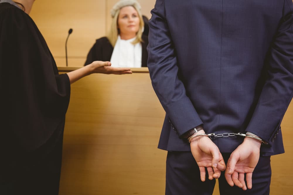 A judge talking with a criminal in handcuffs in the courtroom.