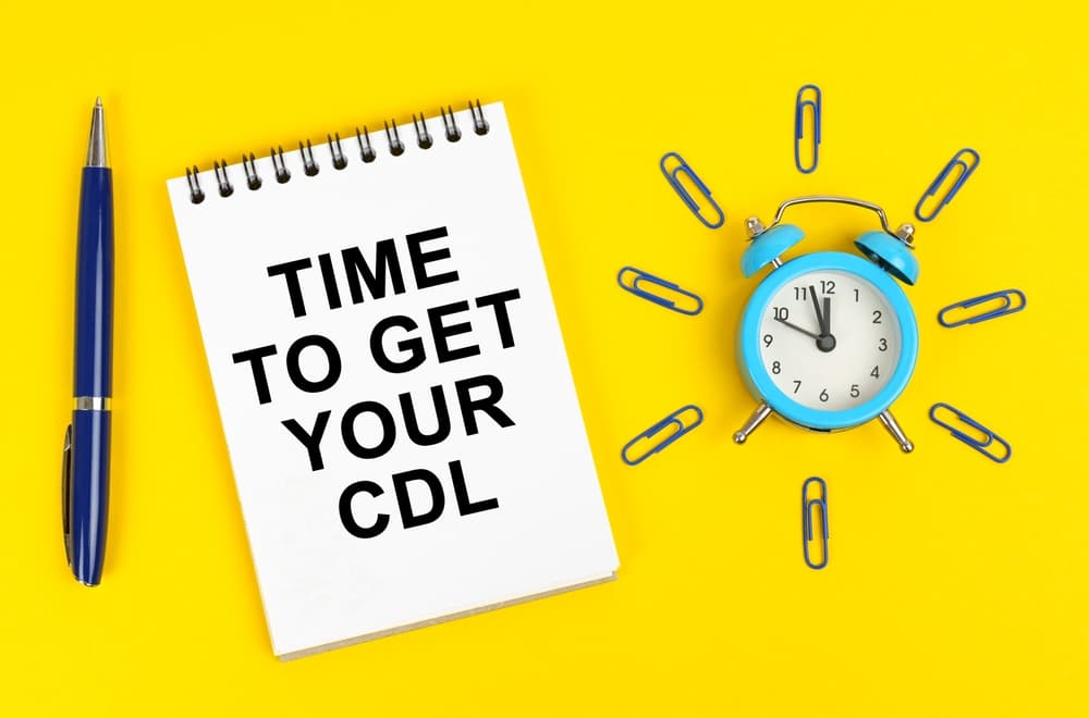 Business concept: On a yellow surface, an alarm clock, a pen, and a notepad with the inscription "Time to Get Your CDL" are arranged, emphasizing urgency and focus.