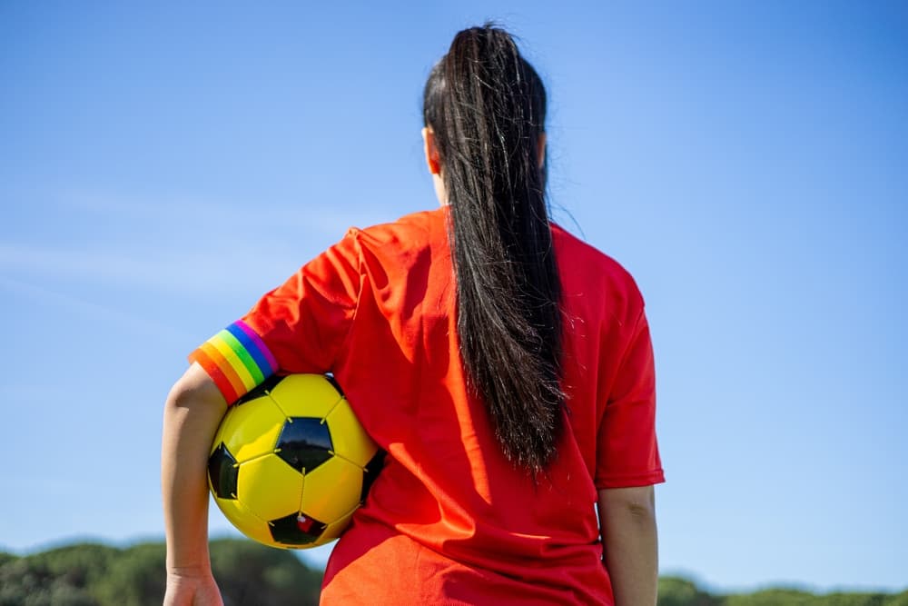 Female soccer player with a pride flag armband on the field, promoting LGBTQ inclusion and combating homophobia in sports.