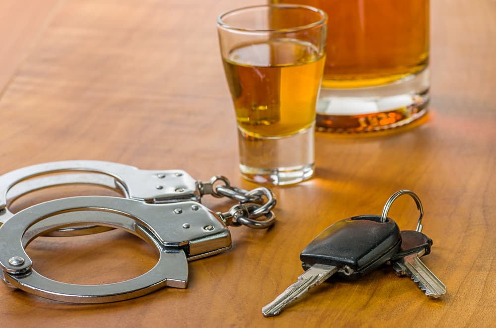 Shot glass with car keys and handcuffs - symbolizing the consequences of drinking and driving.