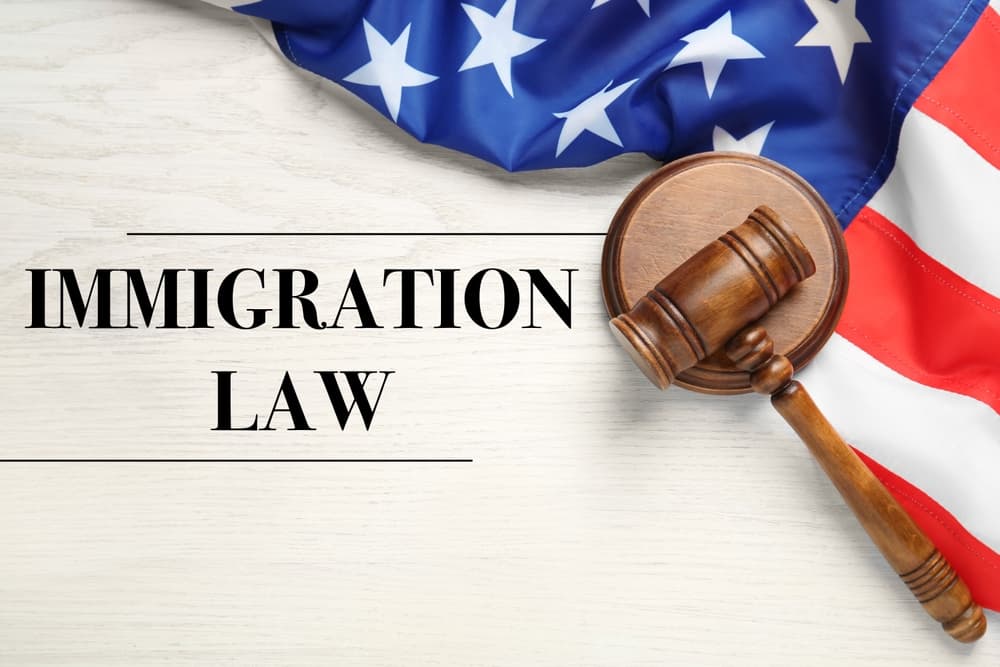 Immigration law concept: Judge's gavel and American flag on a white wooden table, viewed from above.