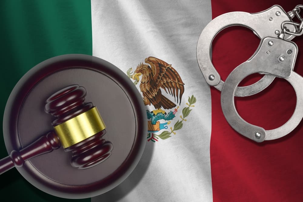 A Mexico flag in a dimly lit room with a judge's gavel and handcuffs. A somber scene symbolizing crime, punishment, and justice in Mexico.