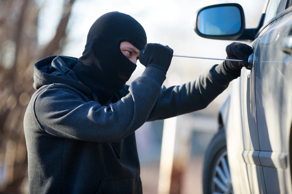 A car thief attempting to unlock the door of a black car.