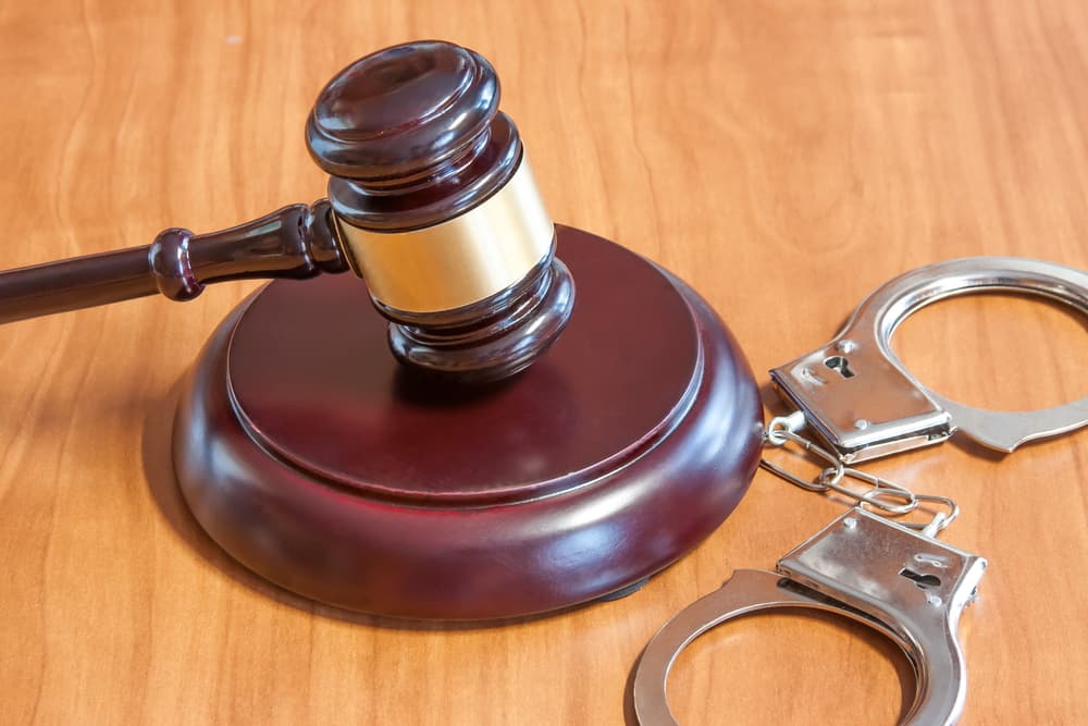 Judge's gavel and handcuffs on a wooden table.