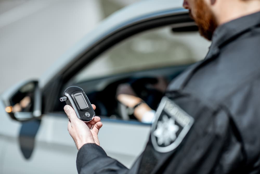 Policeman holding device for checking alcohol intoxication while standing near the stopped car with woman driver